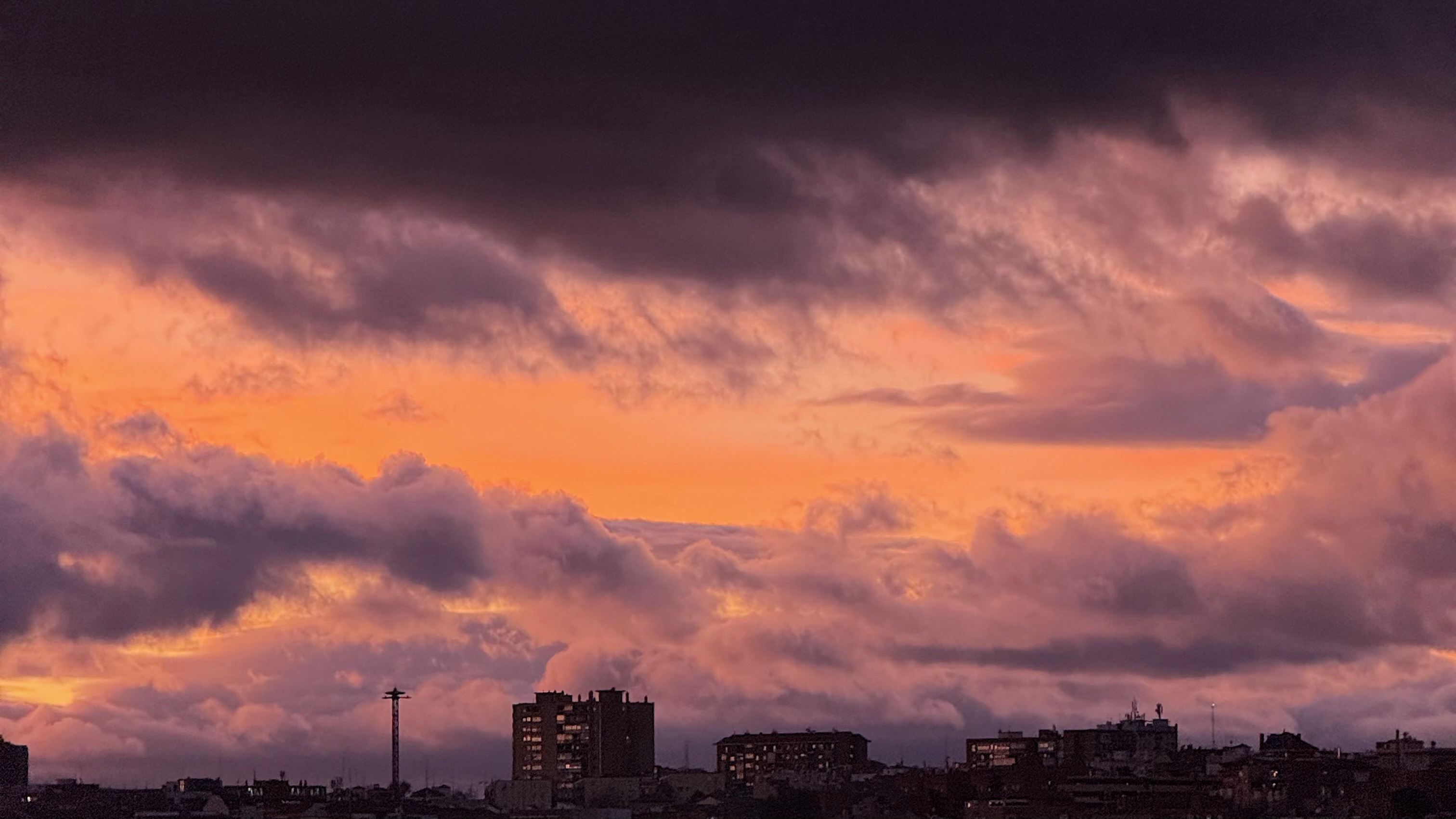City skyline silhouetted against a dramatic sunset sky with orange and purple clouds.